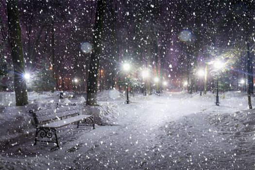 Snowfall in a winter park at night with christmas decorations, lights and  pavement covered with snow. Falling snow.