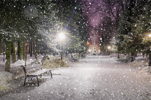 Snowfall in a winter park at night with christmas decorations, lights and  pavement covered with snow. Falling snow.