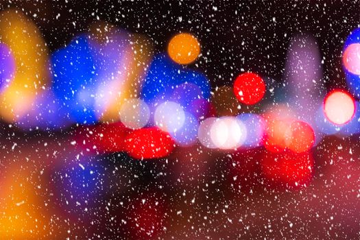 Blurred lights of headlights of cars and lanterns in the night city in a snowfall. Abstract bright bokeh.