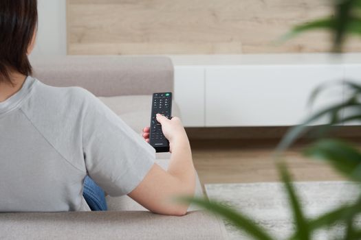 Woman with TV remote control relaxing on sofa in loft apartment