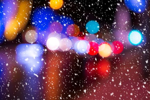 Blurred lights of headlights of cars and lanterns in the night city in a snowfall. Abstract bright bokeh.