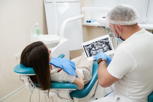 Professional doctor shows to the patient picture of teeth in his medical dental office. Doctor wearing medical clothing.