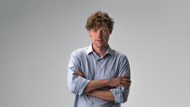 Handsome hipster guy standing with arms folded isolated on light white pastel background. Closeup photo of amazing friendly guy fluffy hairstyle. Studio portrait.