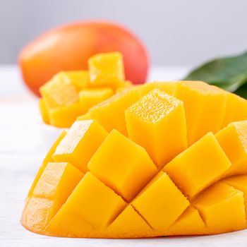 Fresh mango,beautiful chopped fruit with green leaves on bright wooden table background. Tropical fruit design concept, close up, copy space.