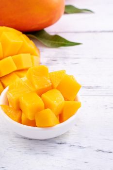 Fresh mango,beautiful chopped fruit with green leaves on bright wooden table background. Tropical fruit design concept, close up, copy space.