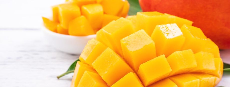 Fresh mango,beautiful chopped fruit with green leaves on bright wooden table background. Tropical fruit design concept, close up, copy space.