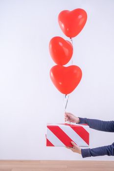 Valentine's day, Mother's day, birthday design concept - Heart helium balloon with gift box on a light wood floor, white wall background, close up.