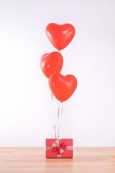 Valentine's day, Mother's day, birthday design concept - Heart helium balloon with gift box on a light wood floor, white wall background, close up.