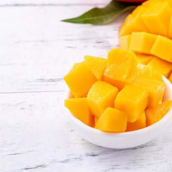 Fresh mango,beautiful chopped fruit with green leaves on bright wooden table background. Tropical fruit design concept, close up, copy space.