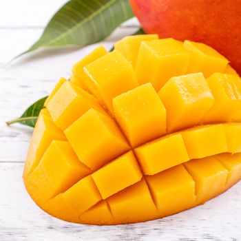 Fresh mango,beautiful chopped fruit with green leaves on bright wooden table background. Tropical fruit design concept, close up, copy space.