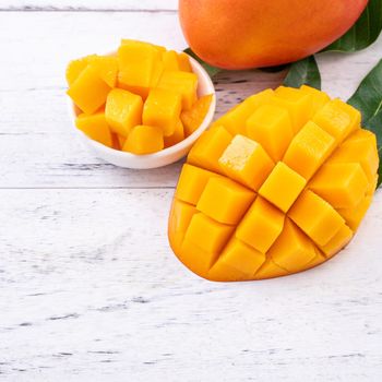 Fresh mango,beautiful chopped fruit with green leaves on bright wooden table background. Tropical fruit design concept, close up, copy space.