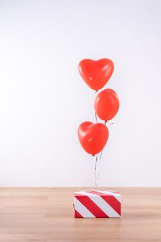 Valentine's day, Mother's day, birthday design concept - Heart helium balloon with gift box on a light wood floor, white wall background, close up.