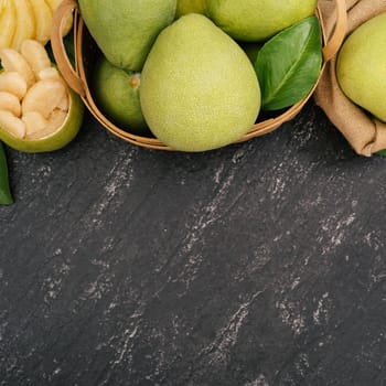 Fresh peeled pomelo, pummelo, grapefruit, shaddock on dark background in bamboo basket. Autumn seasonal fruit, top view, flat lay, tabletop shot.