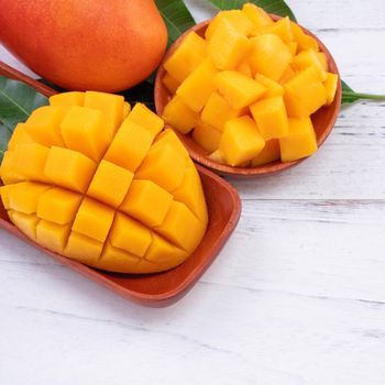 Fresh mango,beautiful chopped fruit with green leaves on bright wooden table background. Tropical fruit design concept, close up, copy space.