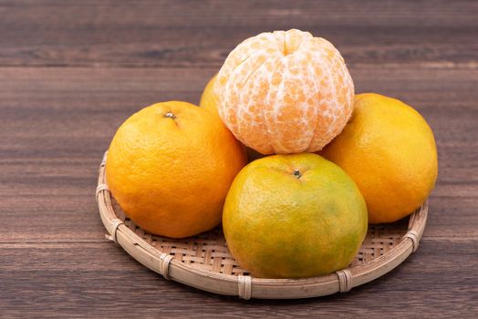 Fresh, beautiful orange color tangerine on bamboo sieve over dark wooden table. Seasonal, traditional fruit of Chinese lunar new year, close up.