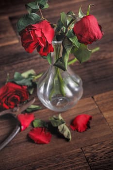 Withered rose on dark gray background and wooden table with fall petals and leaves, design concept of sad Valentine's day romance, broken up, copy,space.