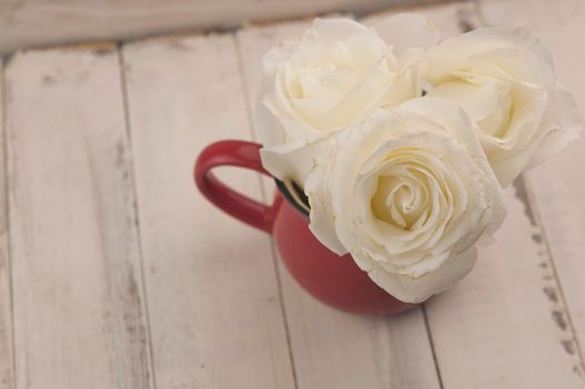 Bouquet of white wedding roses in an old vintage cup on wood background with floral petals