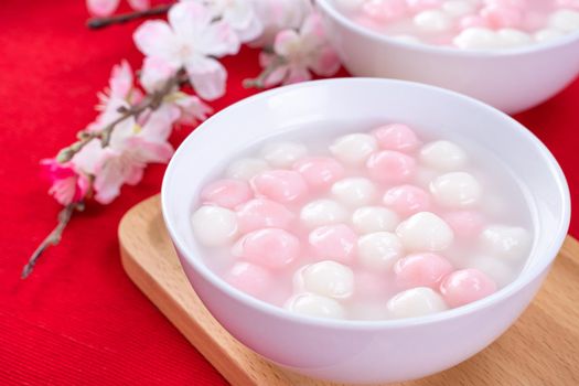 Tang yuan, tangyuan, delicious red and white rice dumpling balls in a small bowl on red background. Asian festive food for Chinese Winter Solstice Festival, close up.