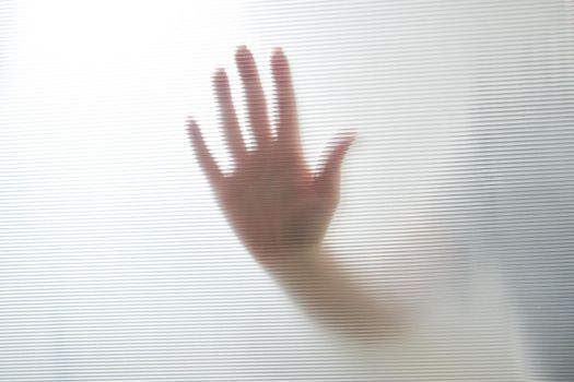 Diffused silhouette of female hands through frosted glass