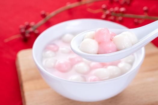 Tang yuan, tangyuan, delicious red and white rice dumpling balls in a small bowl on red background. Asian festive food for Chinese Winter Solstice Festival, close up.