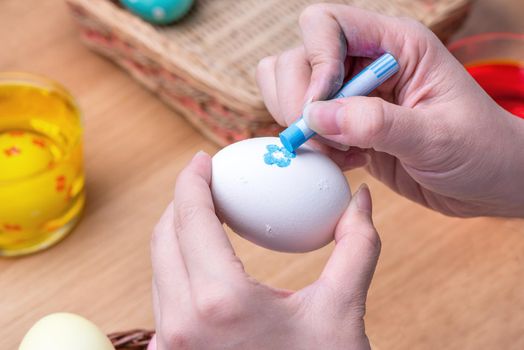 Easter eggs preparation - Young woman is drawing white egg with pastel wax crayon before dyeing colors at home kitchen table, close up, lifestyle