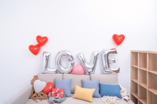 Foil love balloons and gifts on a sofa with white wall in background for Valentine's day, Mother's day surprise design concept.