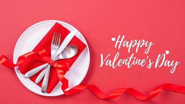 Valentine's Day holiday dating meal, banquet greeting card design concept - White plate with cutlery on red background, top view, flat lay.