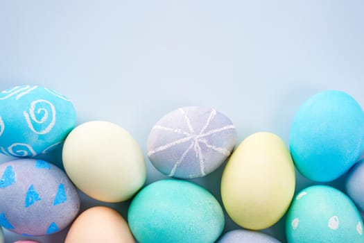 Colorful Easter eggs dyed by colored water with beautiful pattern on a pale blue background, design concept of holiday activity, top view, full frame.