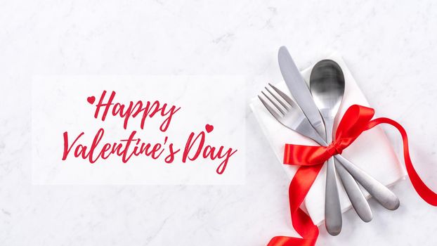 Valentine's Day holiday dating meal, banquet greeting card design concept - White plate and red ribbon on marble background, top view, flat lay.