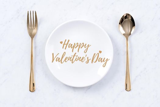 Valentine's Day holiday dating meal, banquet greeting card design concept - White plate and golden color tableware on marble background, top view, flat lay.