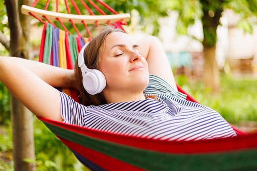 Young woman in headphones listening to music while resting in hammock outdoors.