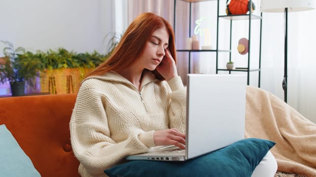 Tired freelancer redhead woman use laptop, suffering from headache problem tension and migraine, stress at home room. Girl works on notebook, sends messages, makes online purchases, watching movies