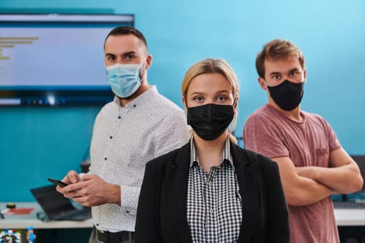 A group of colleagues stand ingin a robotics laboratory, arms crossed, wearing protective masks, symbolizing their teamwork and commitment to technological innovation and scientific research