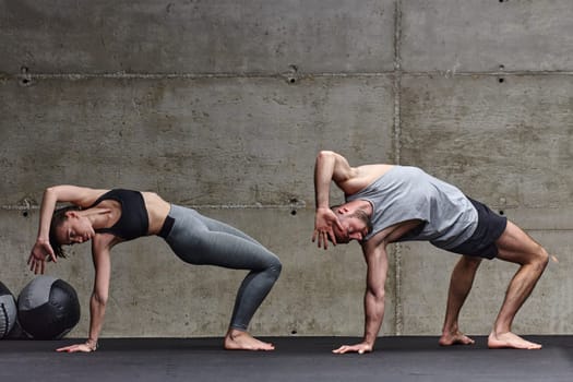 An attractive couple in the gym engaging in various stretching exercises together, showcasing their dedication to fitness, flexibility, and overall wellbeing. With synchronized movements, they demonstrate coordination, balance, and endurance while supporting and motivating each other on their fitness journey.