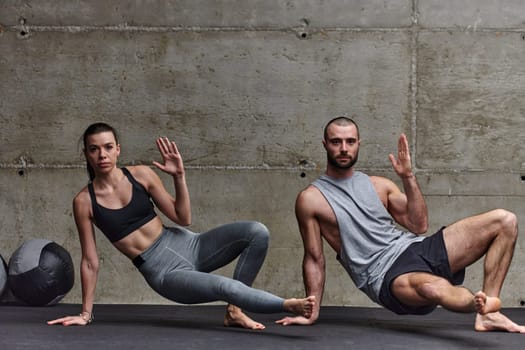 An attractive couple in the gym engaging in various stretching exercises together, showcasing their dedication to fitness, flexibility, and overall wellbeing. With synchronized movements, they demonstrate coordination, balance, and endurance while supporting and motivating each other on their fitness journey.