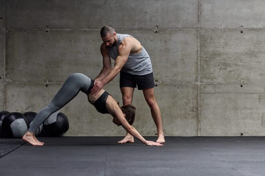 A muscular man assisting a fit woman in a modern gym as they engage in various body exercises and muscle stretches, showcasing their dedication to fitness and benefiting from teamwork and support.