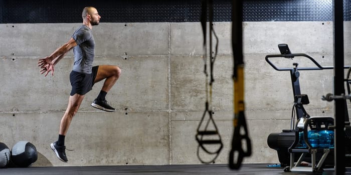 A muscular man captured in air as he jumps in a modern gym, showcasing his athleticism, power, and determination through a highintensity fitness routine.