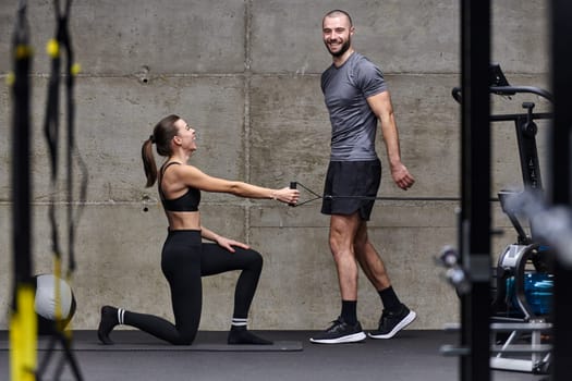 A muscular man assisting a fit woman in a modern gym as they engage in various body exercises and muscle stretches, showcasing their dedication to fitness and benefiting from teamwork and support.