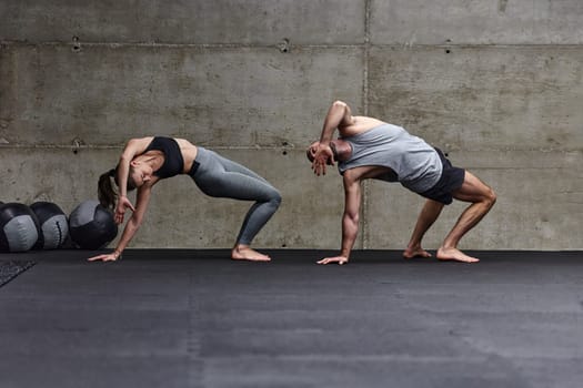 An attractive couple in the gym engaging in various stretching exercises together, showcasing their dedication to fitness, flexibility, and overall wellbeing. With synchronized movements, they demonstrate coordination, balance, and endurance while supporting and motivating each other on their fitness journey.