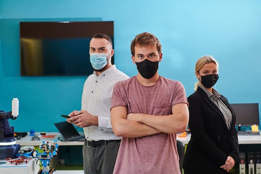 A group of colleagues stand ingin a robotics laboratory, arms crossed, wearing protective masks, symbolizing their teamwork and commitment to technological innovation and scientific research