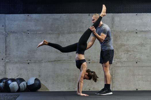 A muscular man assisting a fit woman in a modern gym as they engage in various body exercises and muscle stretches, showcasing their dedication to fitness and benefiting from teamwork and support.