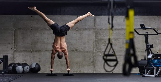 A muscular man in a handstand position, showcasing his exceptional balance and body control while performing a variety of exercises to enhance his overall body stability and strength in a modern gym.