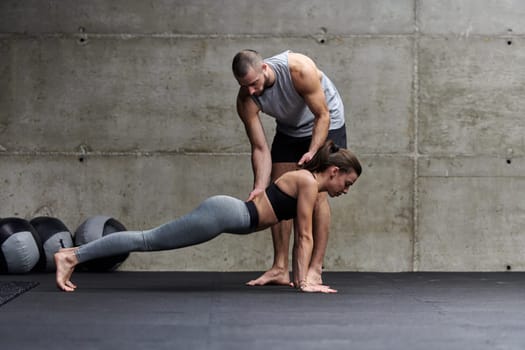 A muscular man assisting a fit woman in a modern gym as they engage in various body exercises and muscle stretches, showcasing their dedication to fitness and benefiting from teamwork and support.