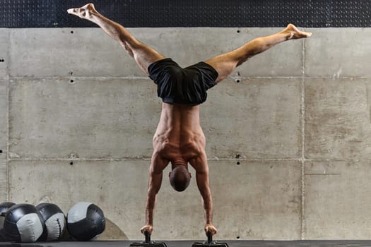 A muscular man in a handstand position, showcasing his exceptional balance and body control while performing a variety of exercises to enhance his overall body stability and strength in a modern gym.