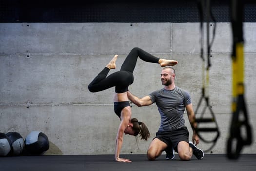 A muscular man assisting a fit woman in a modern gym as they engage in various body exercises and muscle stretches, showcasing their dedication to fitness and benefiting from teamwork and support.