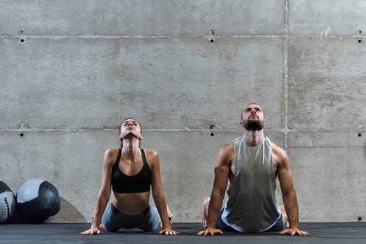 An attractive couple in the gym engaging in various stretching exercises together, showcasing their dedication to fitness, flexibility, and overall wellbeing. With synchronized movements, they demonstrate coordination, balance, and endurance while supporting and motivating each other on their fitness journey.