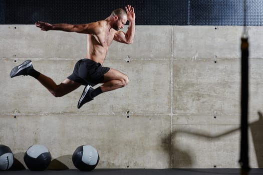 A muscular man captured in air as he jumps in a modern gym, showcasing his athleticism, power, and determination through a highintensity fitness routine.