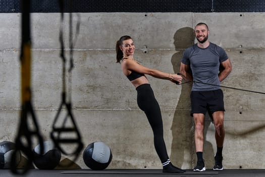 A muscular man assisting a fit woman in a modern gym as they engage in various body exercises and muscle stretches, showcasing their dedication to fitness and benefiting from teamwork and support.