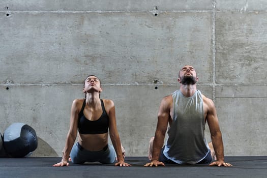 An attractive couple in the gym engaging in various stretching exercises together, showcasing their dedication to fitness, flexibility, and overall wellbeing. With synchronized movements, they demonstrate coordination, balance, and endurance while supporting and motivating each other on their fitness journey.