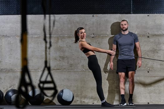 A muscular man assisting a fit woman in a modern gym as they engage in various body exercises and muscle stretches, showcasing their dedication to fitness and benefiting from teamwork and support.